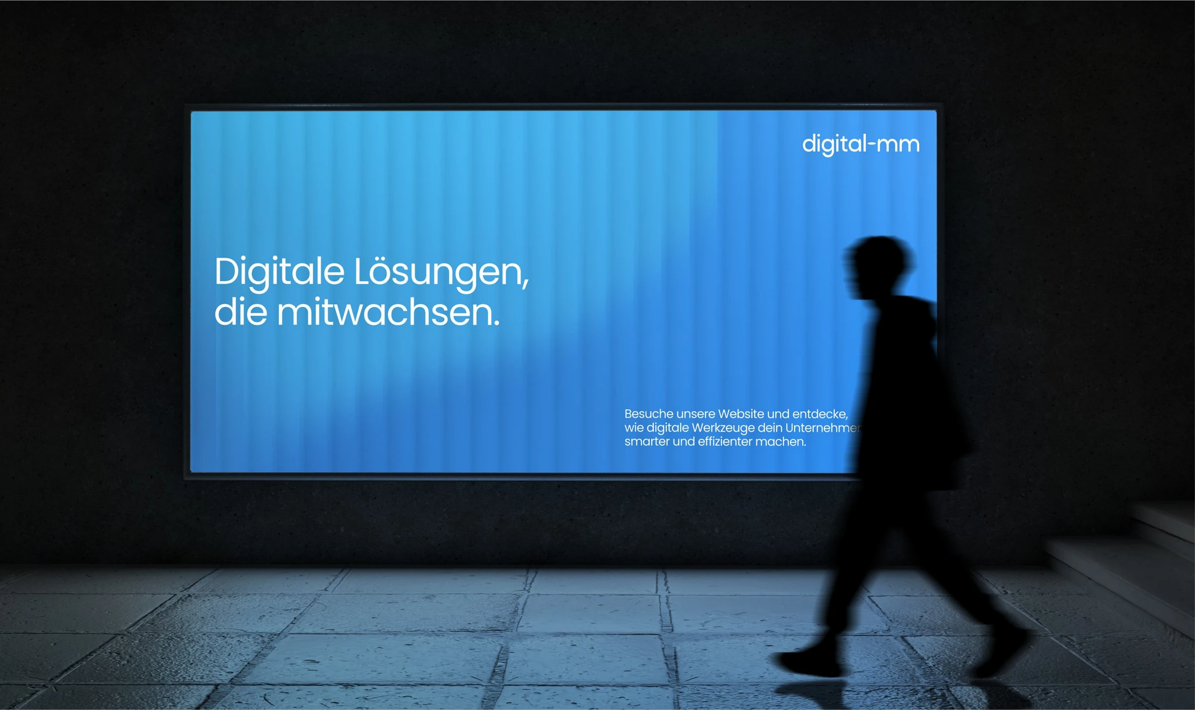 Billboard digital-mm w ciemnym przejściu, obok przechodzi sylwetka człowieka